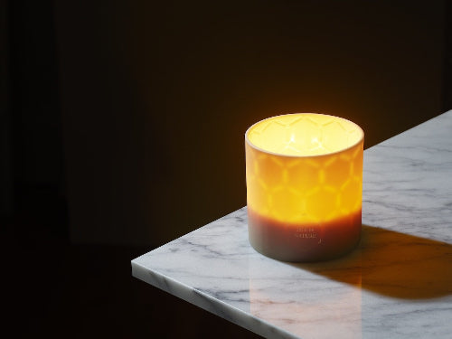 Beeswax candle with a Caribbean island design, lit and glowing softly.