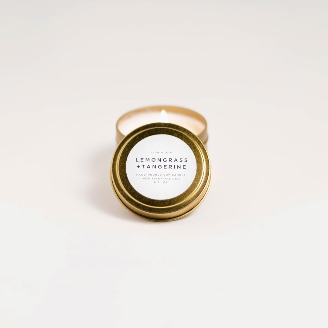 Lemongrass tangerine soy candle in a small brushed gold travel tin with lit wick.