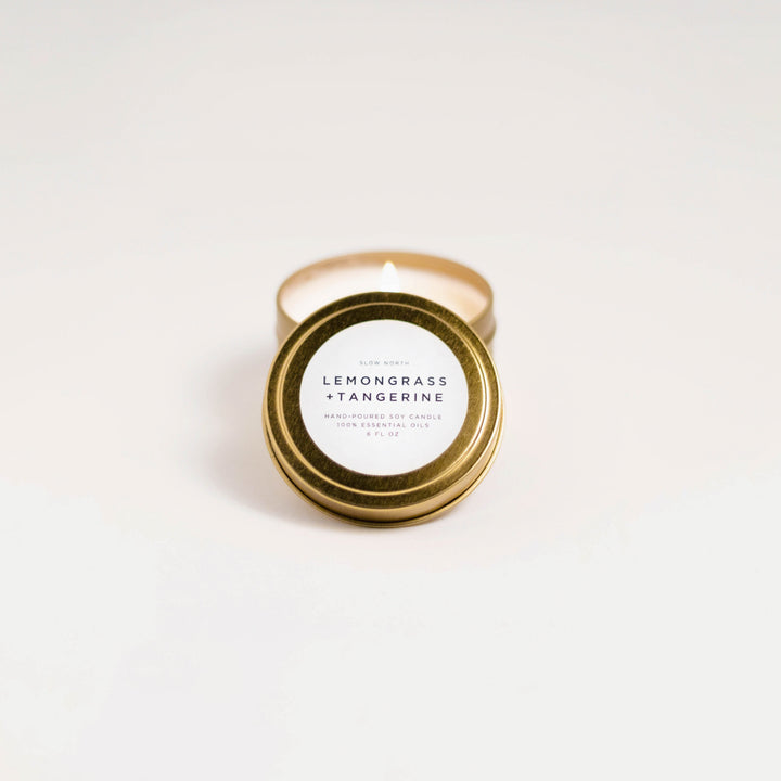Lemongrass tangerine soy candle in a small brushed gold travel tin with lit wick.