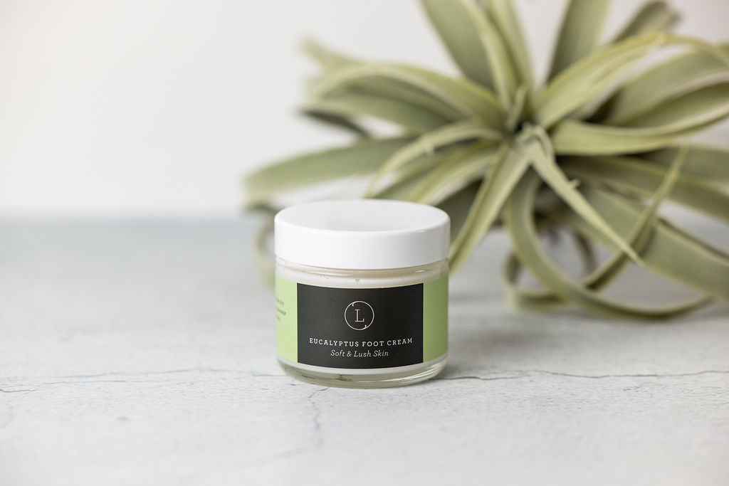 Jar of eucalyptus shea butter foot cream with eucalyptus leaves and shea butter.