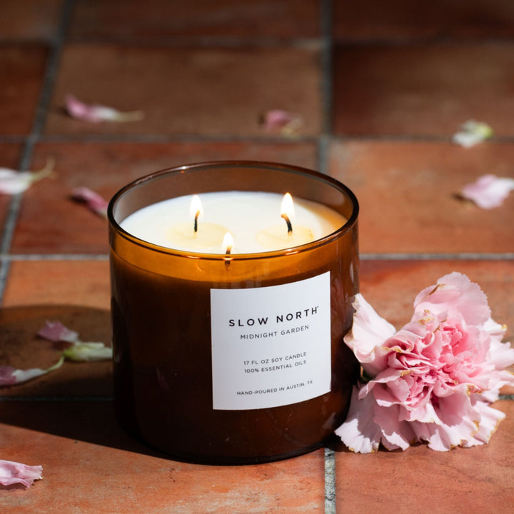 Midnight Garden three-wick candle burning in a glass jar with a floral background.
