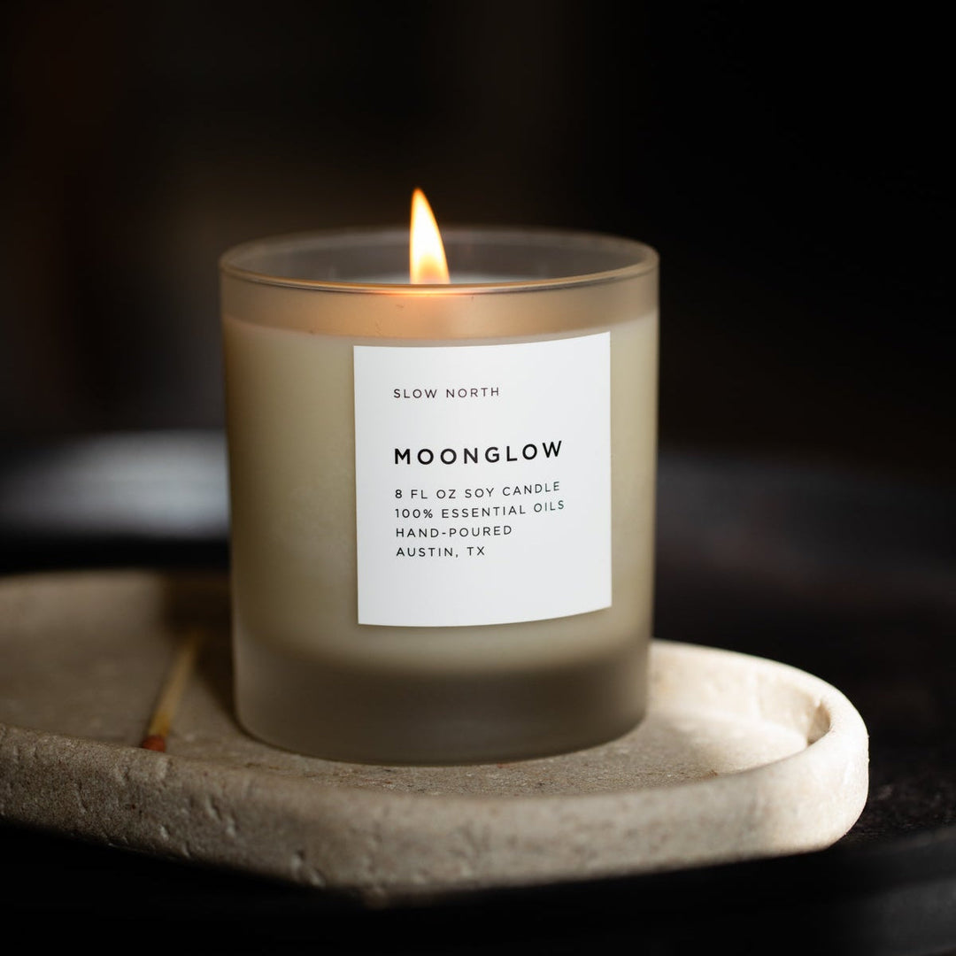 Moonglow signature candle with lit flame and warm earthy scent.