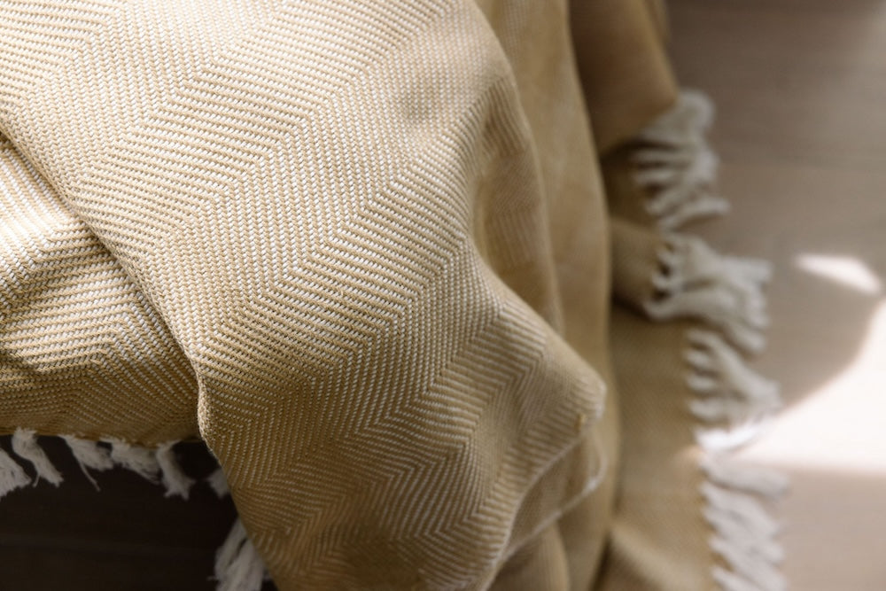 Close-up of the almond herringbone weave and white fringe.