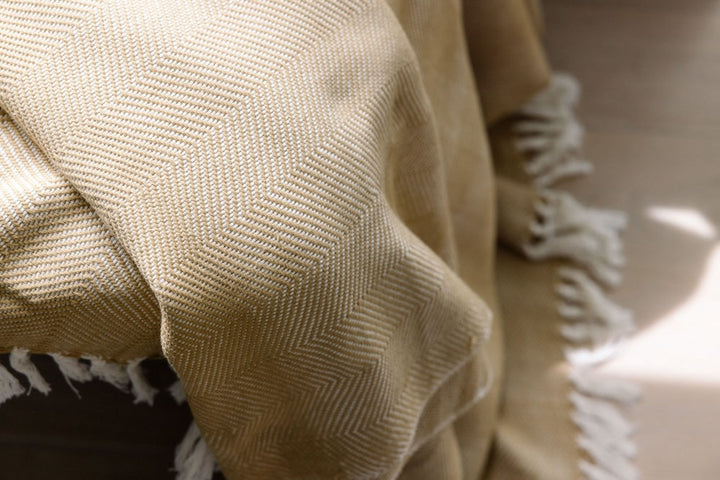 Close-up of the almond herringbone weave and white fringe.