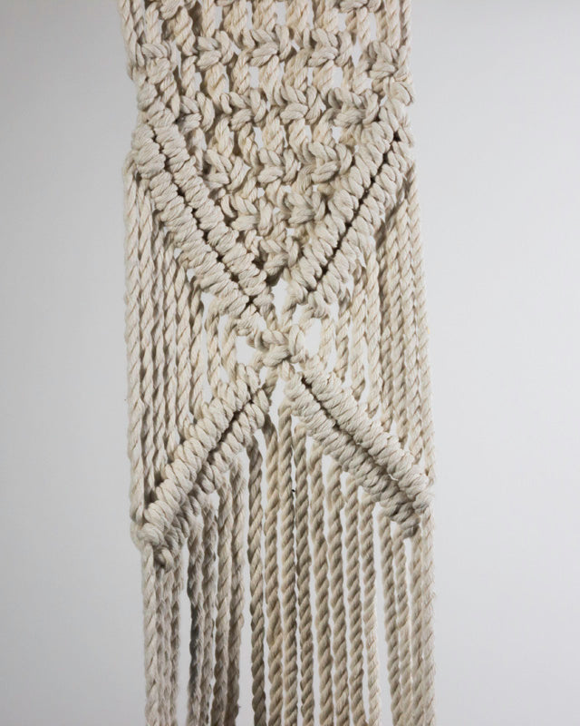 White macrame plant holder with an intricate knotted design.
