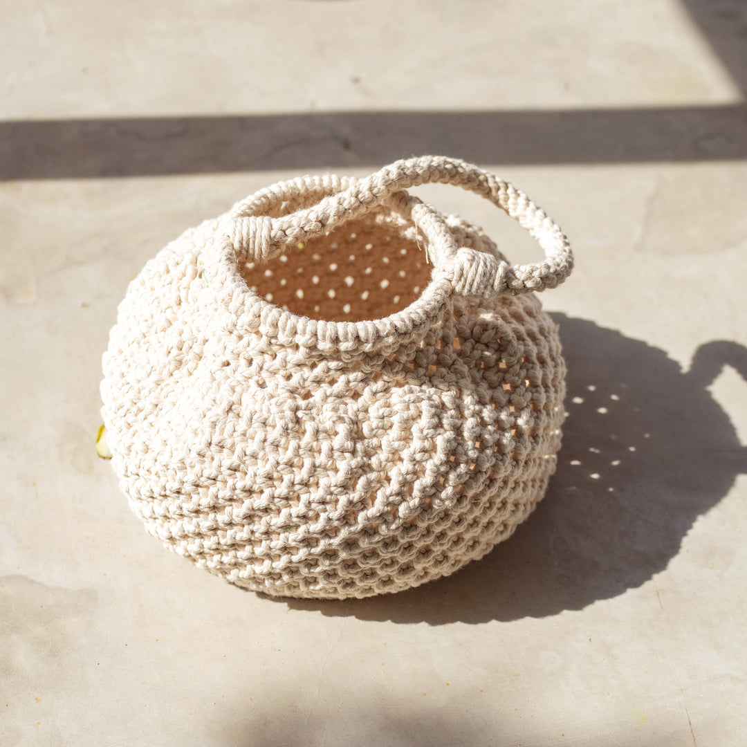 Off-white macrame bucket bag with a woven design and drawstring closure, displayed against a neutral background.