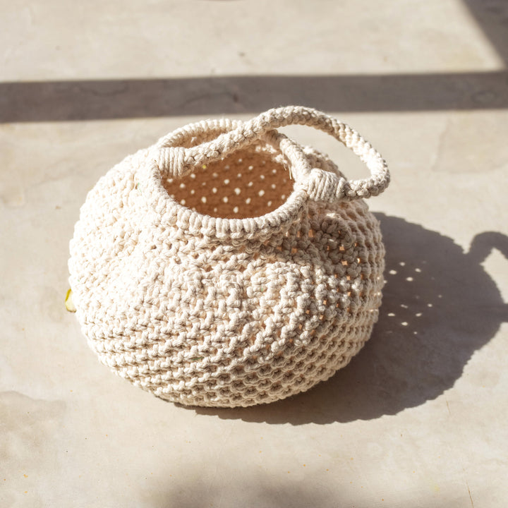 Off-white macrame bucket bag with a woven design and drawstring closure, displayed against a neutral background.
