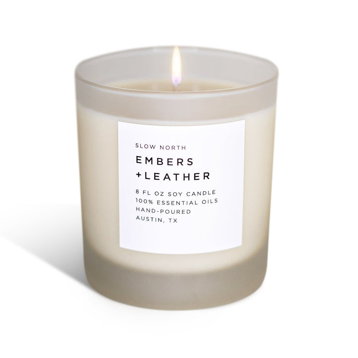 Embers &amp; Leather signature candle in a glass jar with textured leather label and warm flame.
