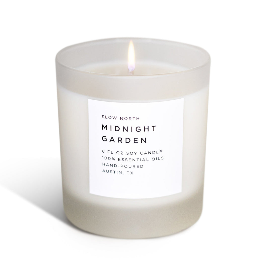 Midnight Garden signature candle with lush floral design and soft flame in a glass jar.