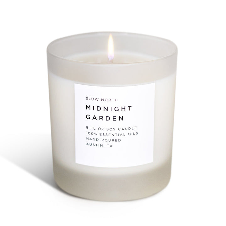 Midnight Garden signature candle with lush floral design and soft flame in a glass jar.