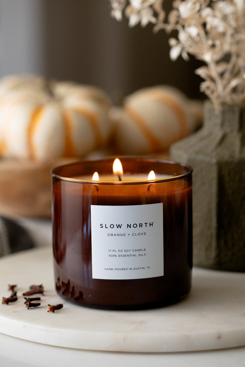Orange clove three-wick candle with vibrant orange wax and burning wicks.