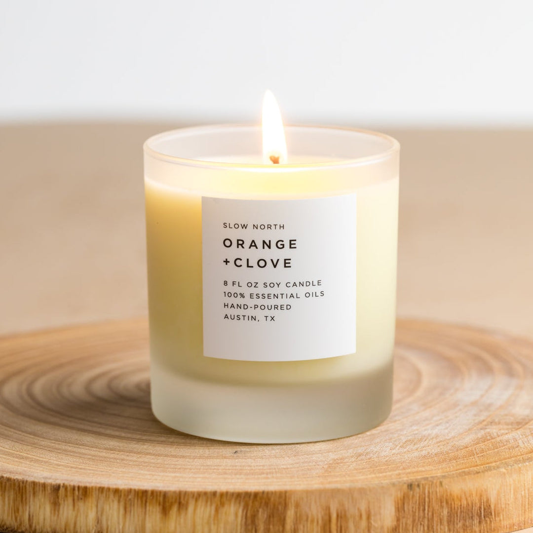 Orange clove soy candle with lit flame and natural wax finish.