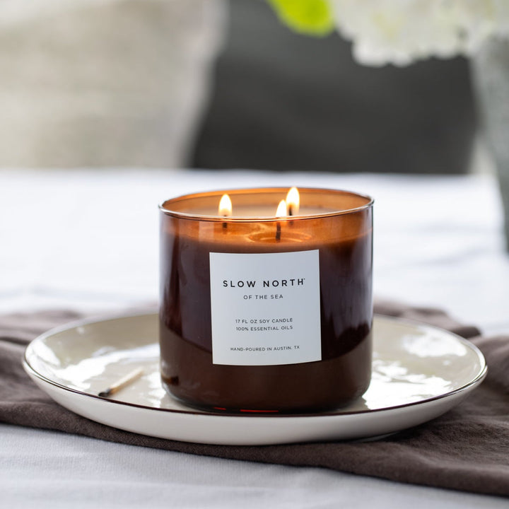 Of The Sea three-wick candle in a glass jar with natural soy wax and lit wicks.