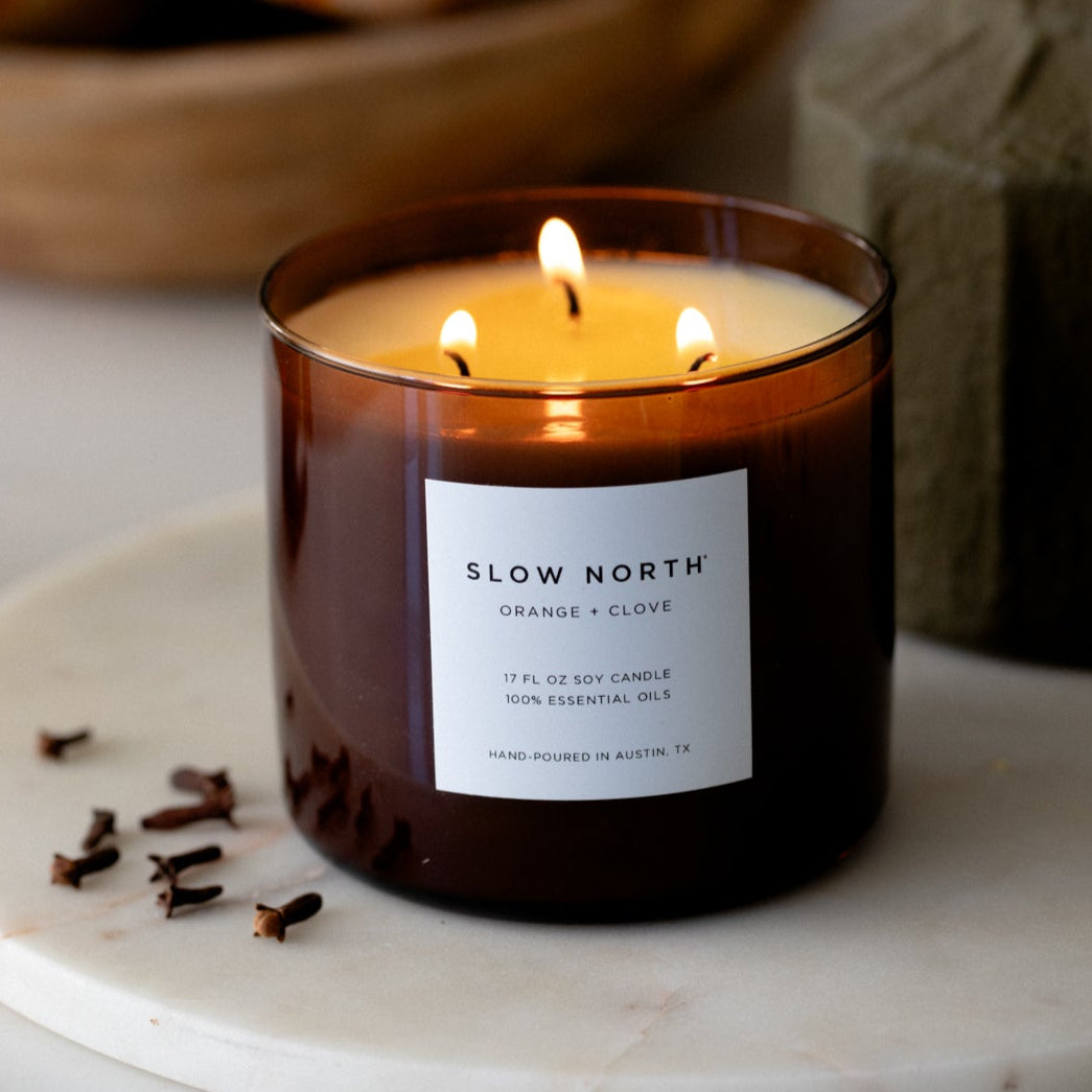 Orange Clove three-wick candle in a glass jar with three wicks and warm glow.