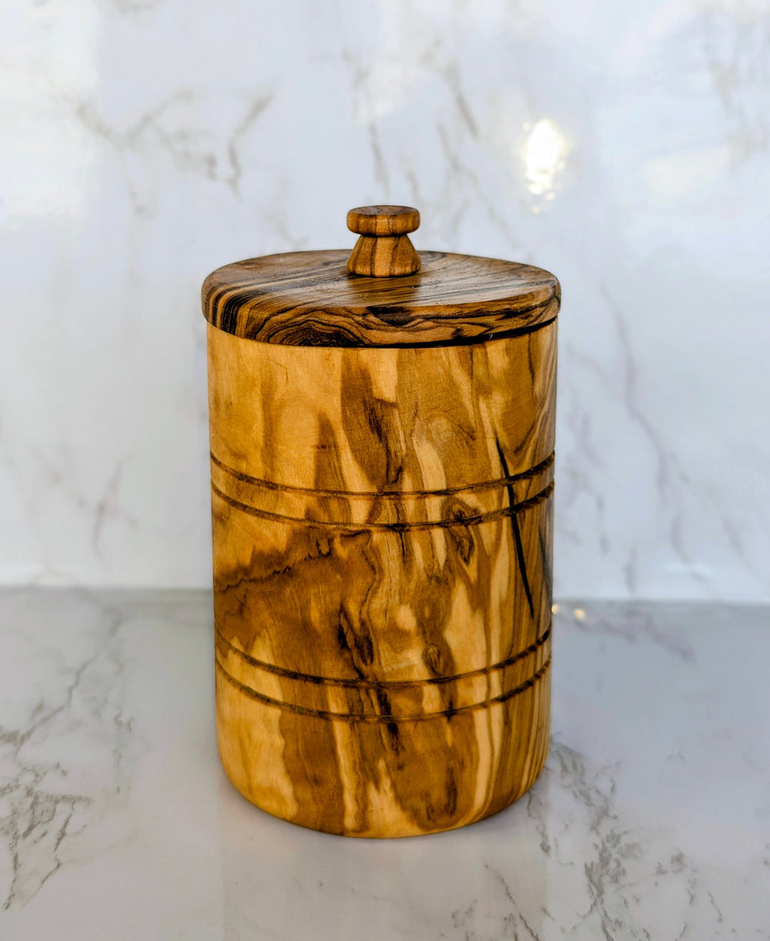 Hand-carved olive wood spice jar with lid, showcasing detailed wood grain and a smooth, natural finish.