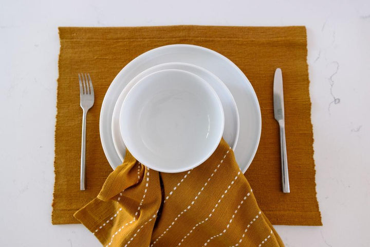 Bronze cocktail napkin on a placemat under a white plate and cutlery