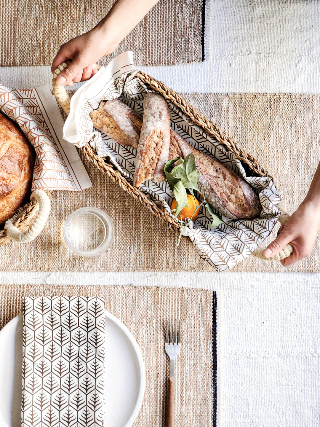 Handwoven seagrass bread basket with white handles, shown as a set of two