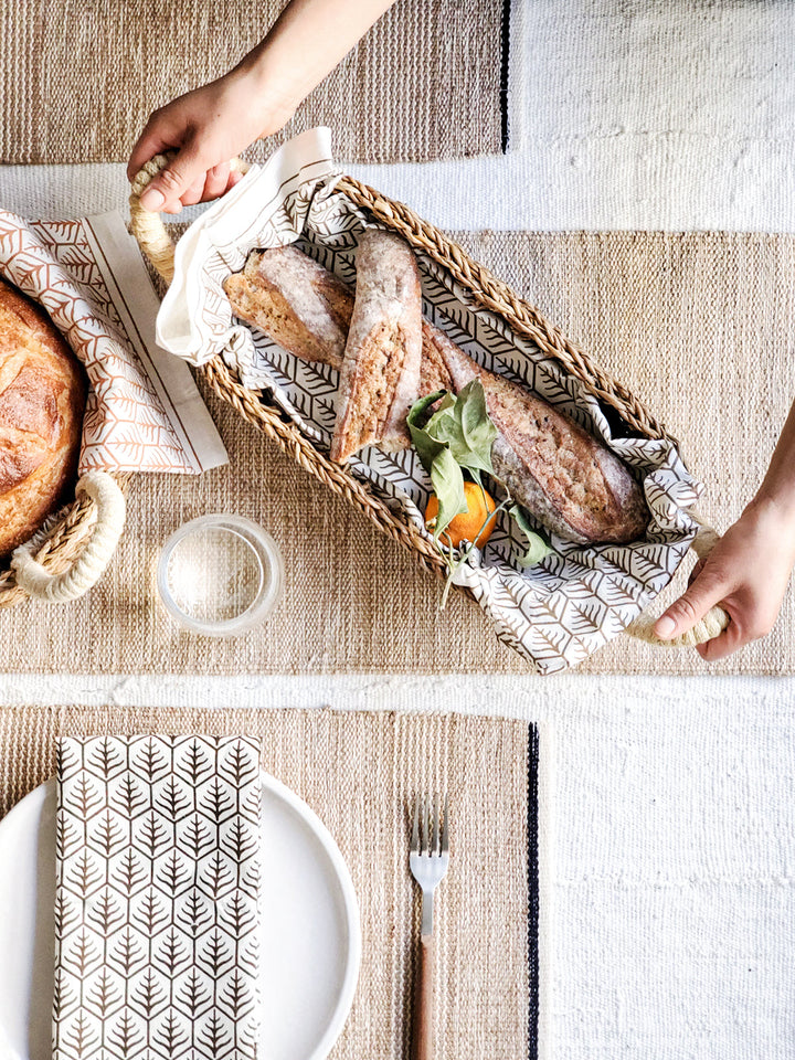 Handwoven seagrass bread basket with white handles, shown as a set of two