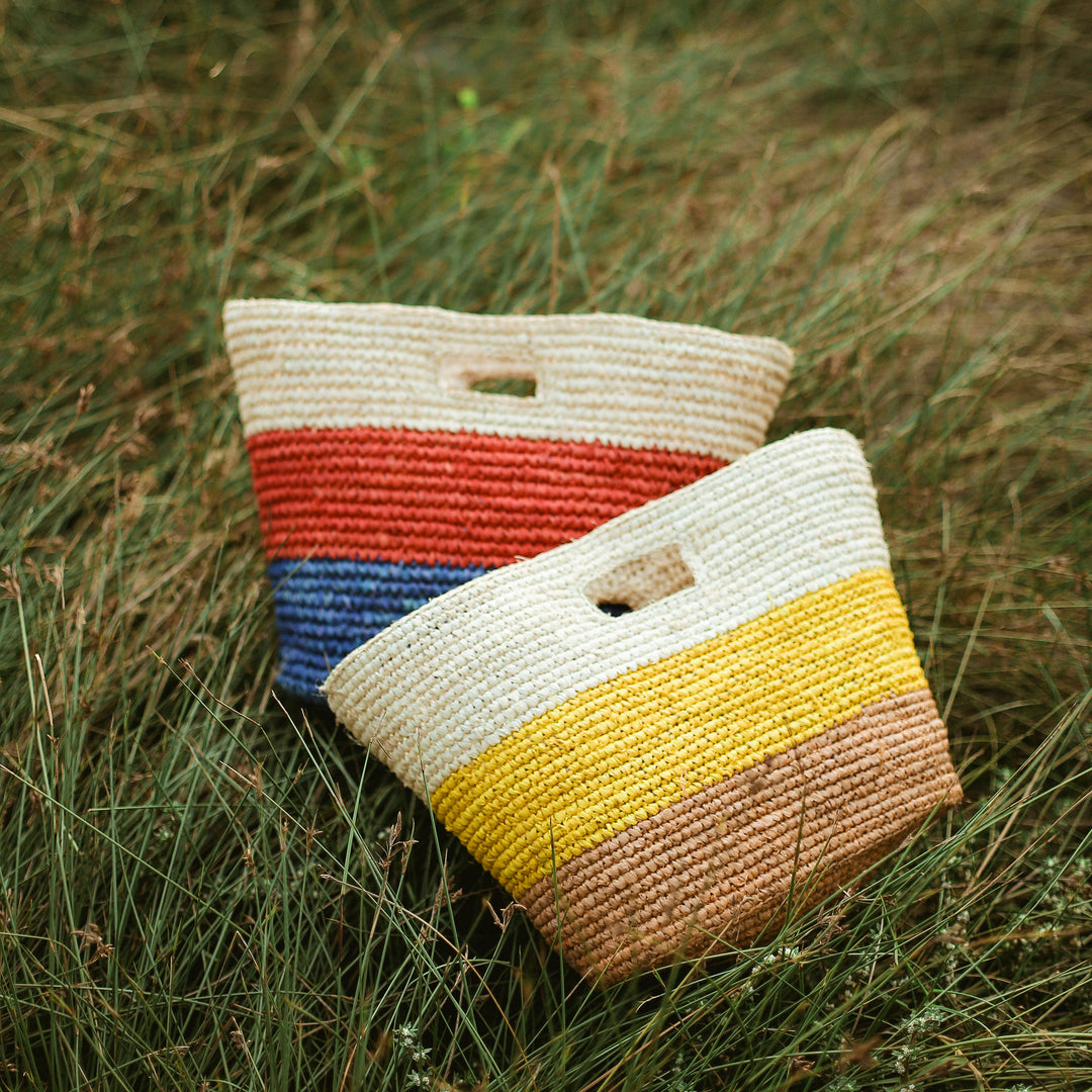 Yellow and beige raffia tote bag with woven handles, shown in a stylish, natural-fiber design.
