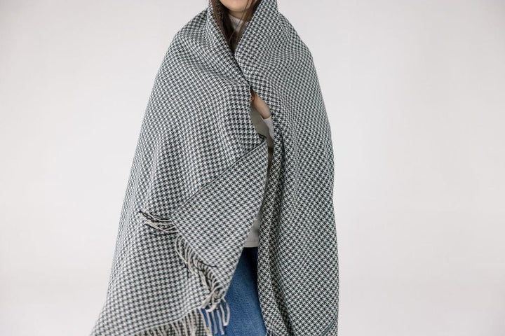 Person wrapped in the slate and white pinwheel cotton throw, fringe hanging at the edges.