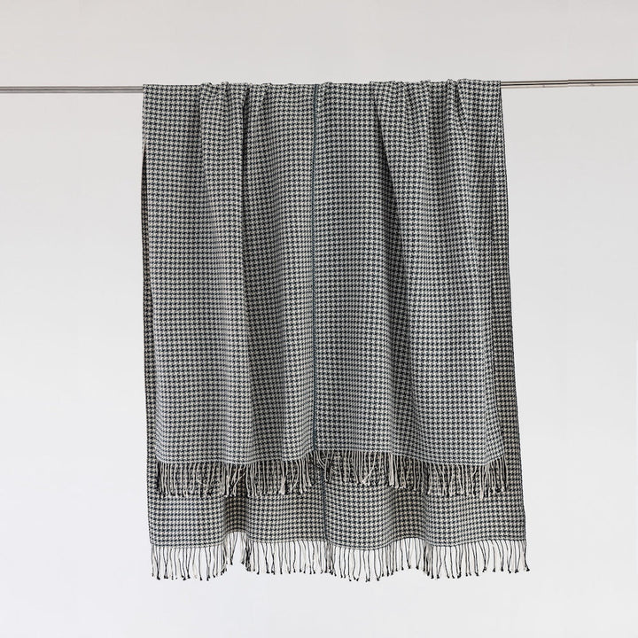 Slate and white pinwheel check cotton throw hanging from a metal rail against a pale wall, with hand-tied fringe.
