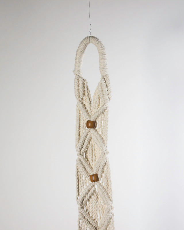 White macrame plant holder with intricate knot detail for a potted plant.