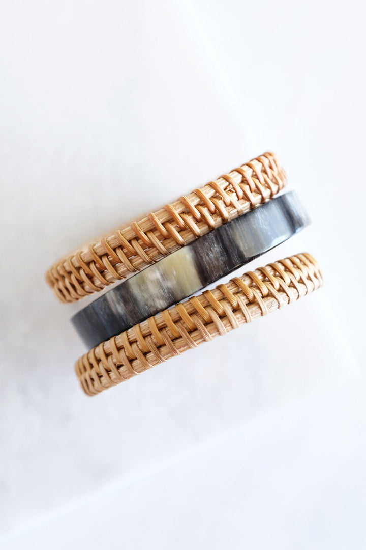 Set of buffalo horn and rattan bangles on a neutral background.