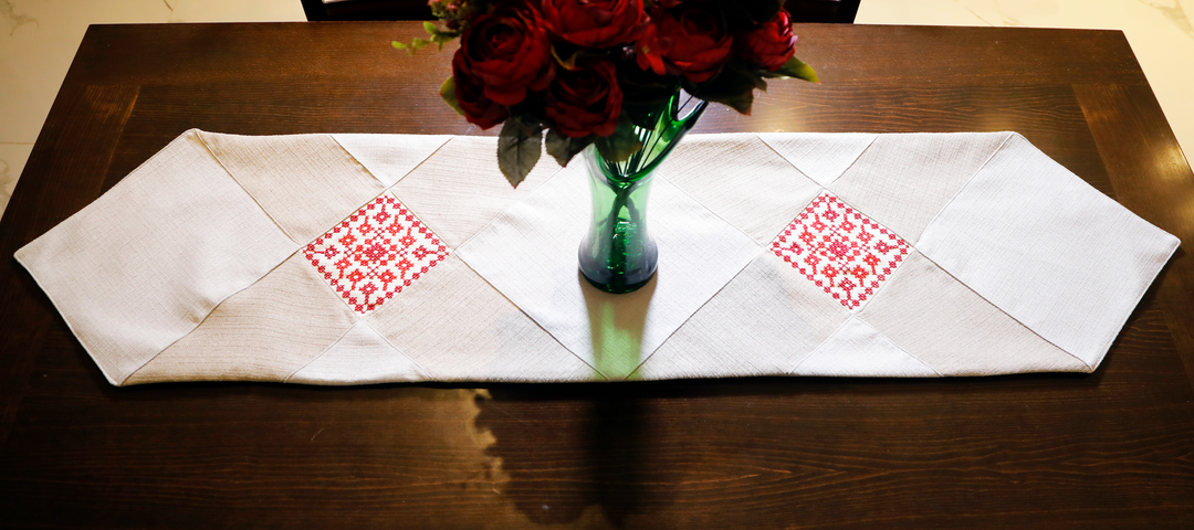 Natural Palestinian table runner with red tatreez, styled on a wooden coffee table.