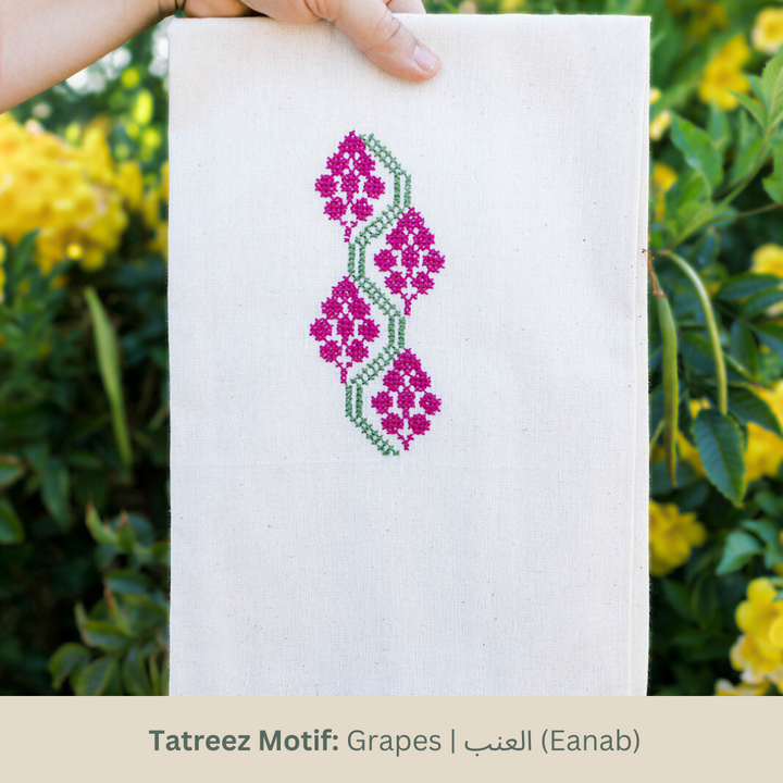 Hand-embroidered tea towel with the Grapes tatreez motif in magenta and green on natural cotton.