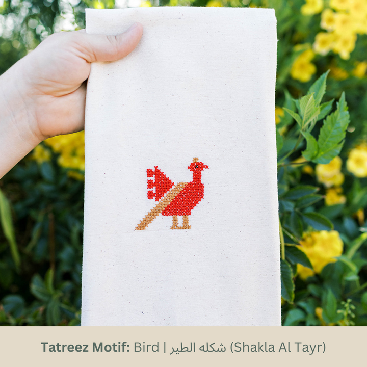 Hand-embroidered tea towel with the Bird tatreez motif, a red and tan rooster on natural cotton.