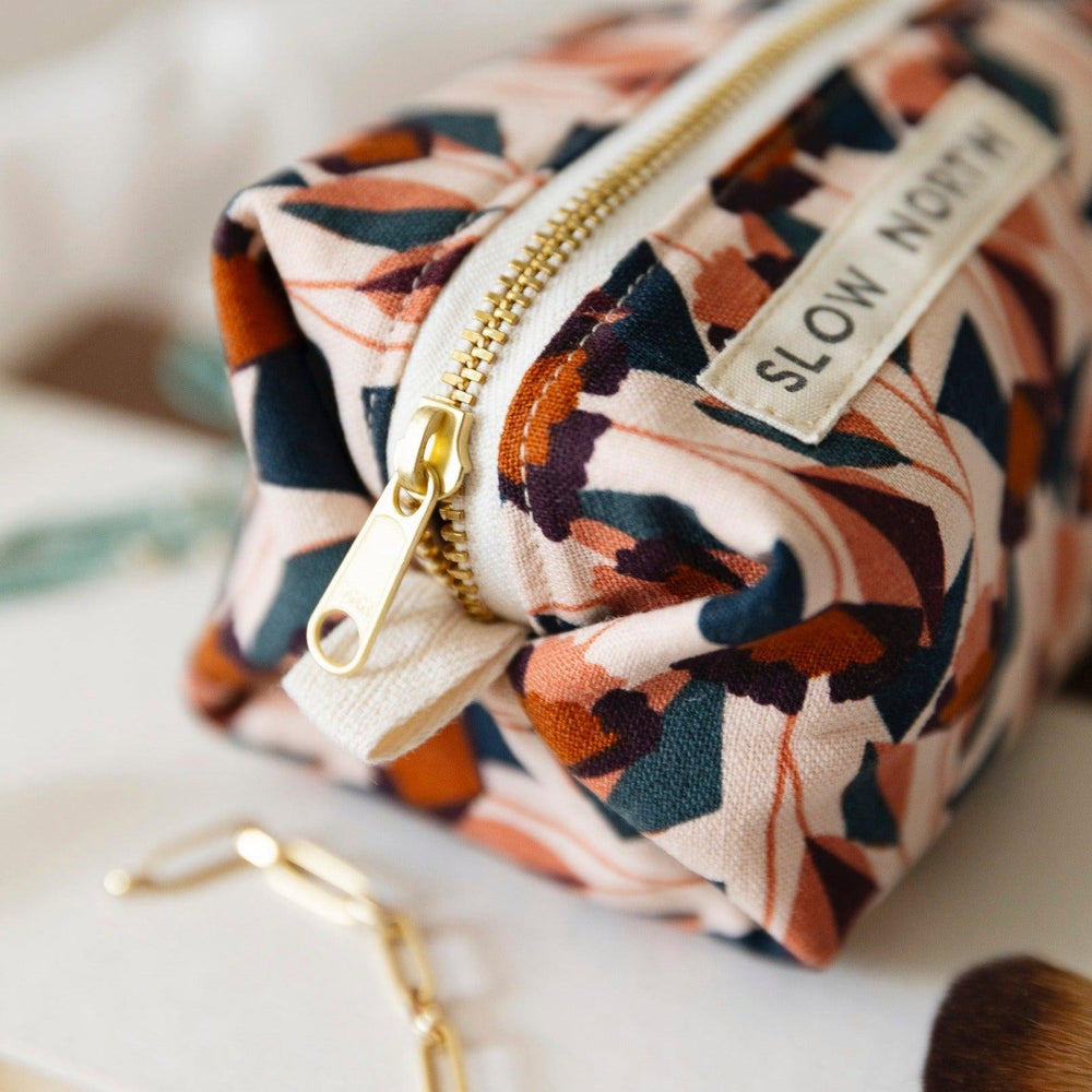 Blush cotton-linen pouch with floral design and brass zipper closure.