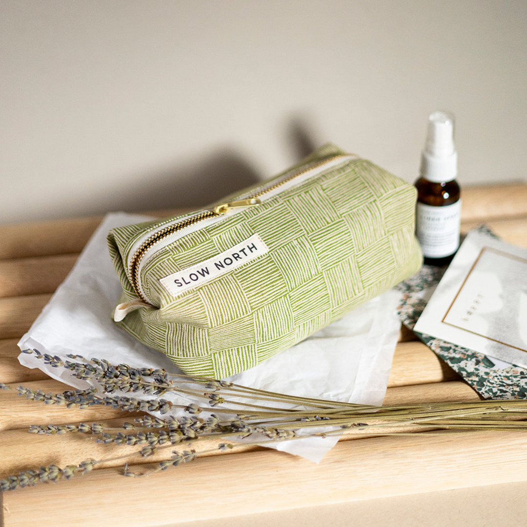 Green cotton-linen pouch with self-standing structure and brass zipper closure.