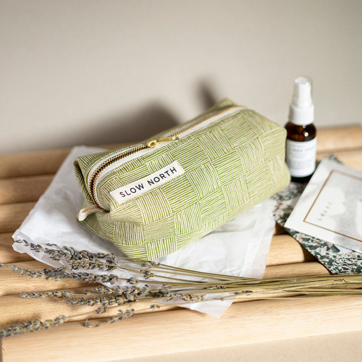 Green cotton-linen pouch with self-standing structure and brass zipper closure.