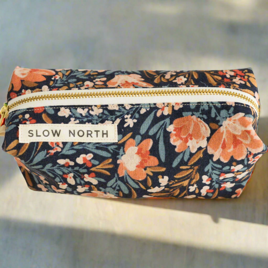 Pom Blossom travel pouch with floral cotton-linen exterior and pink and white pom-pom accents.