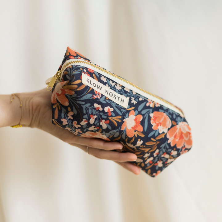 Travel pouch with pom-pom accents shown on a neutral background.