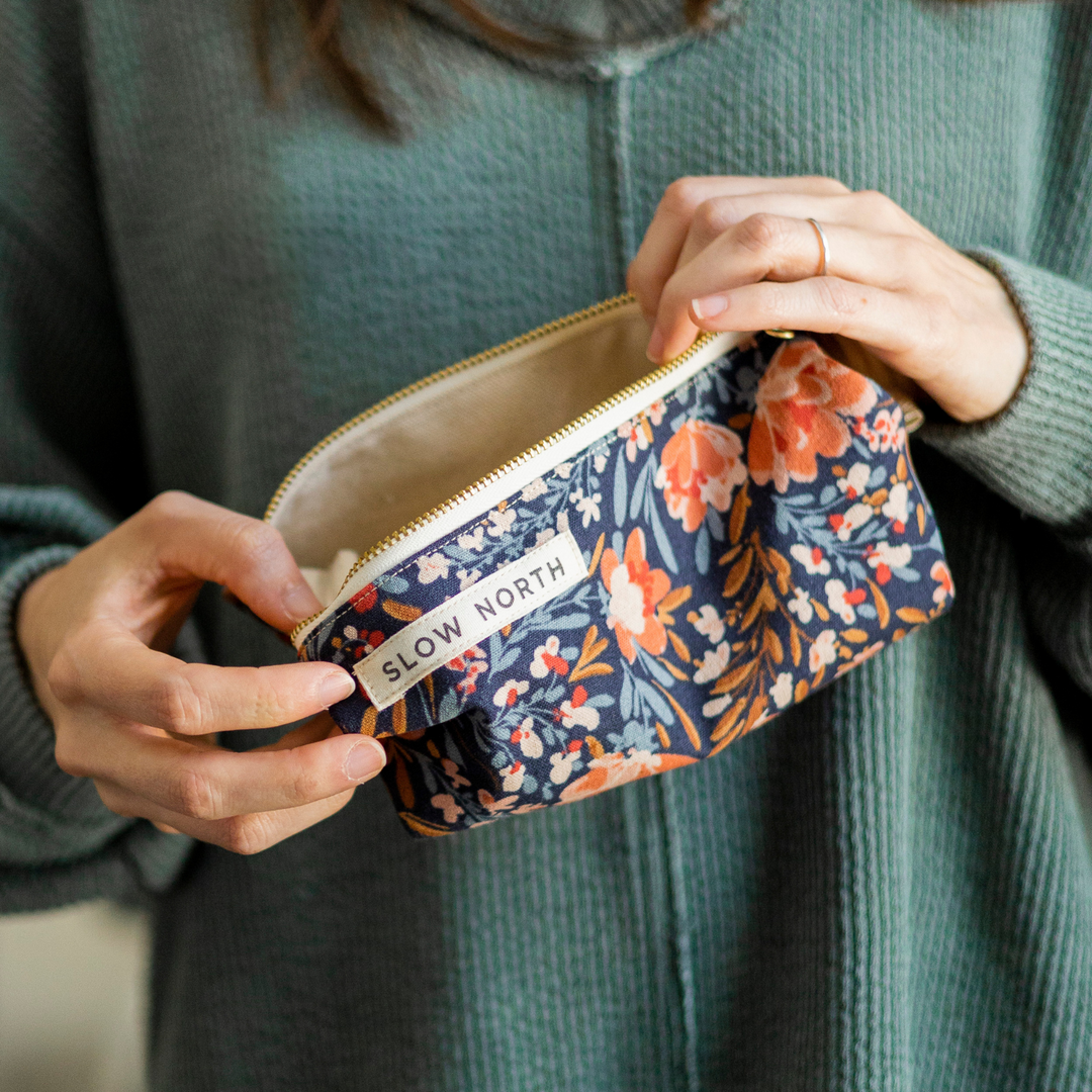 Cotton-linen pouch with floral print and decorative pom-pom trim.