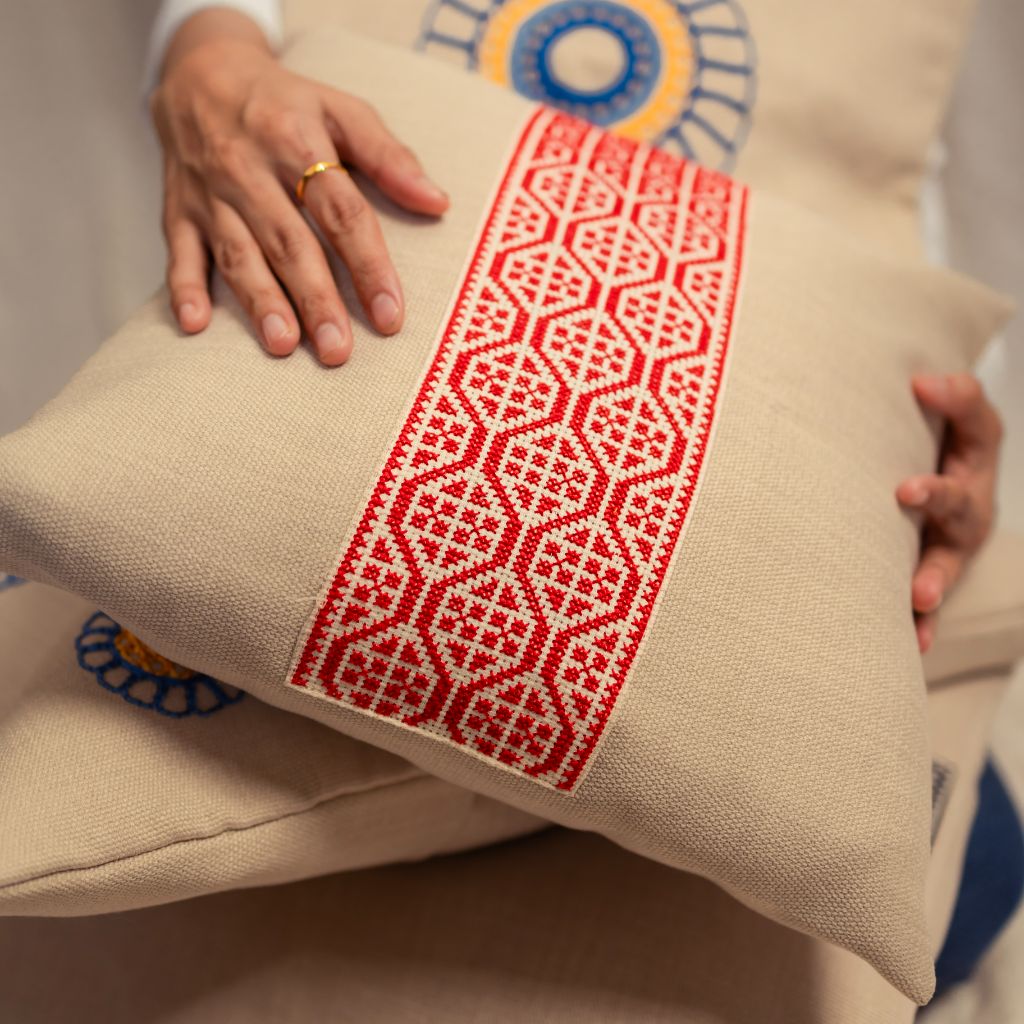 Red geometric tatreez band across a natural oatmeal cushion cover.