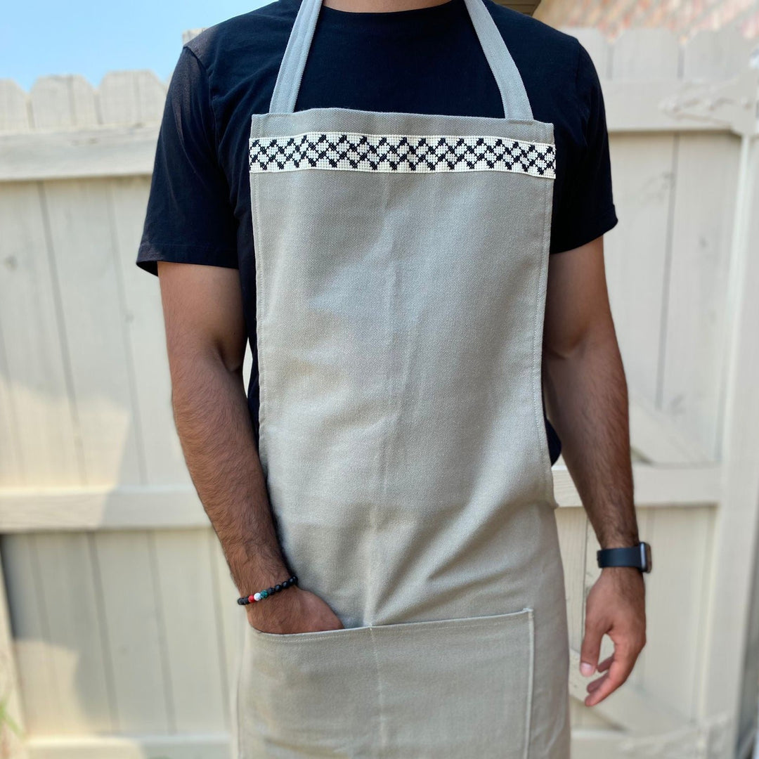Hand-embroidered grey full-length apron with a black-and-white kuffiyeh pattern, made in Palestine.