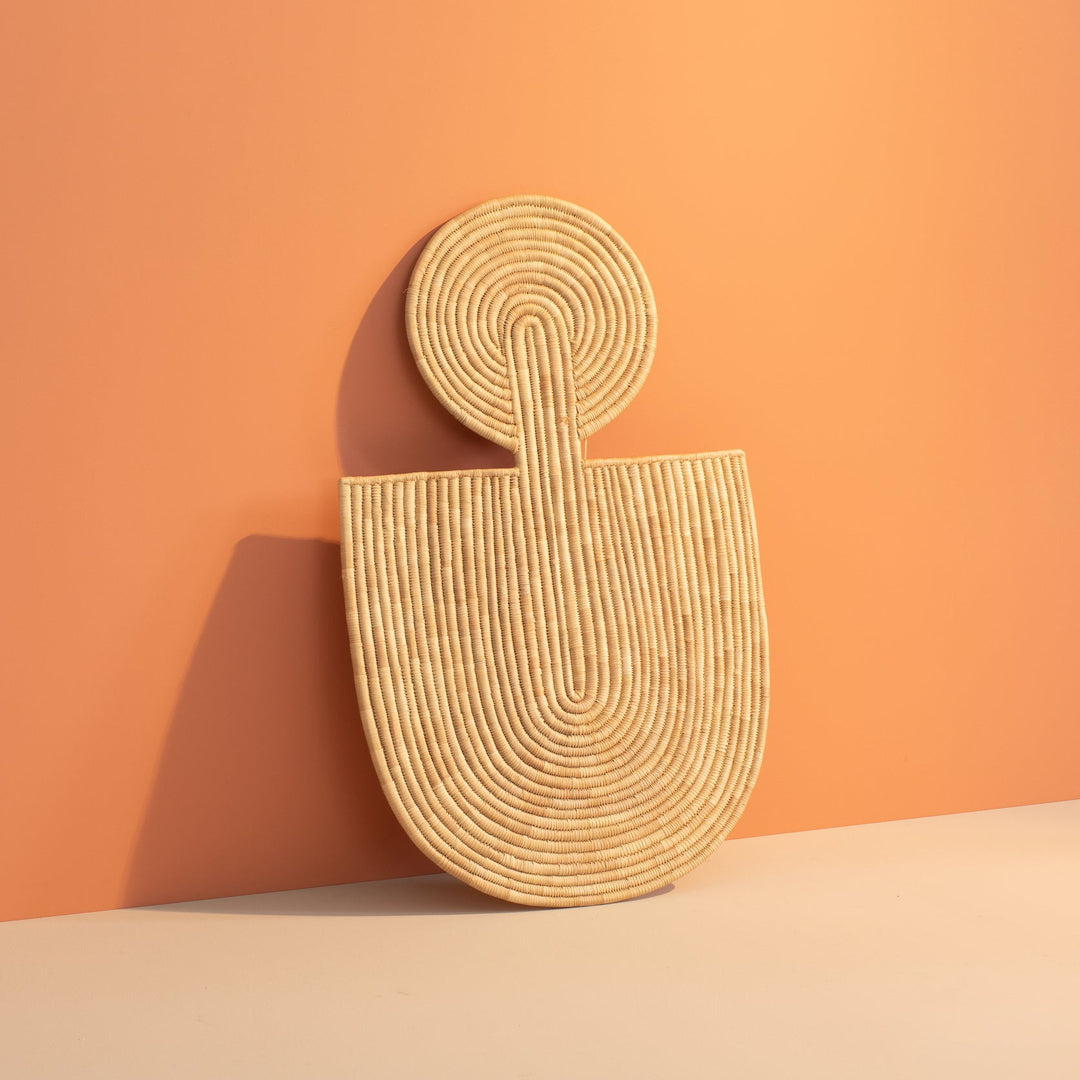 All-natural woven wall mask with a round coiled disc top and U-shaped body, handcrafted from undyed fiber.