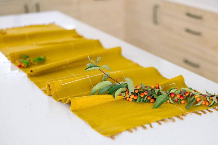 A mustard cotton table runner running the length of a white kitchen island with a berry branch.