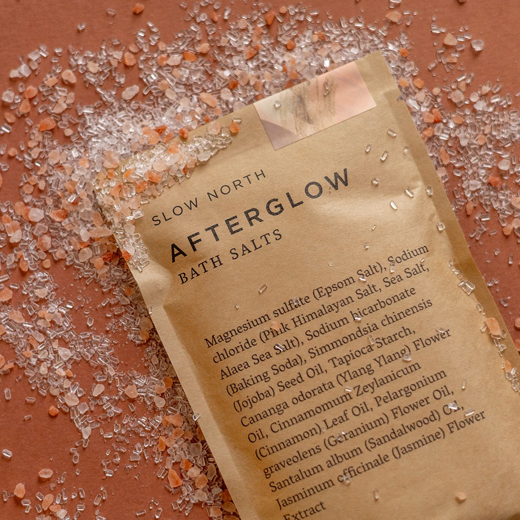 Kraft pouch of Afterglow bath salts with floral essential oil blend and visible colorful salt crystals.