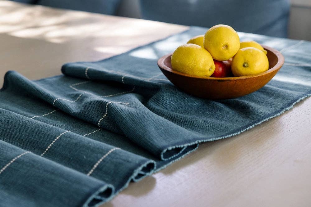 A teal cotton table runner on a wooden table with a bowl of lemons.
