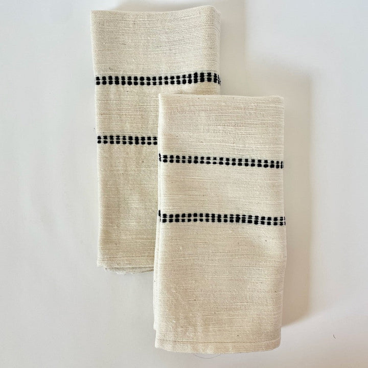 Pair of natural handwoven Ethiopian cotton dinner napkins with a black woven check band, folded, on a white background