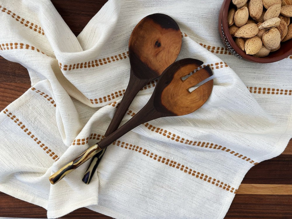Natural cotton napkin with a bronze check band under wooden spoons and a bowl of nuts