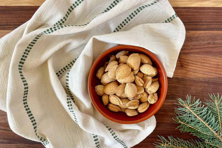 Natural cotton napkin with a cedar green check band wrapped around a bowl of almonds on a wooden board