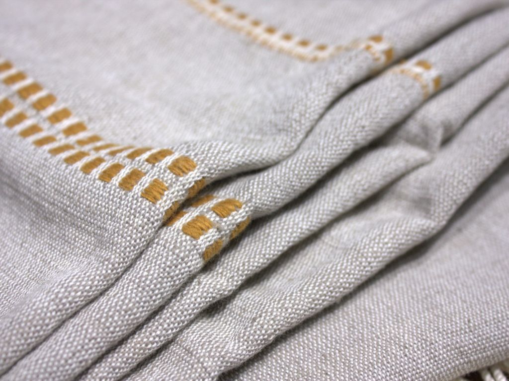 Close-up of the stone cotton throw folded, showing the gold woven motif along the edge.