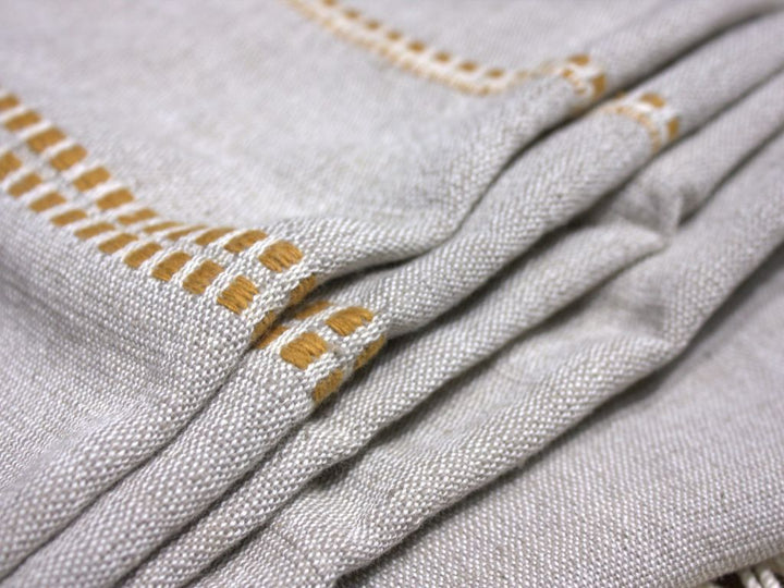 Close-up of the stone cotton throw folded, showing the gold woven motif along the edge.