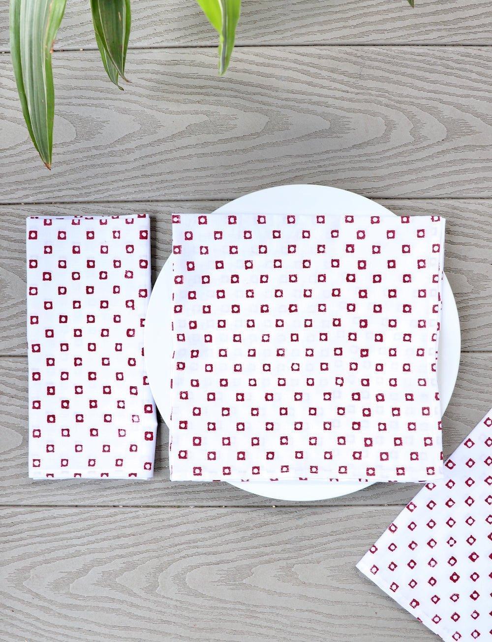 Set of four cotton napkins with a red square block print, folded.