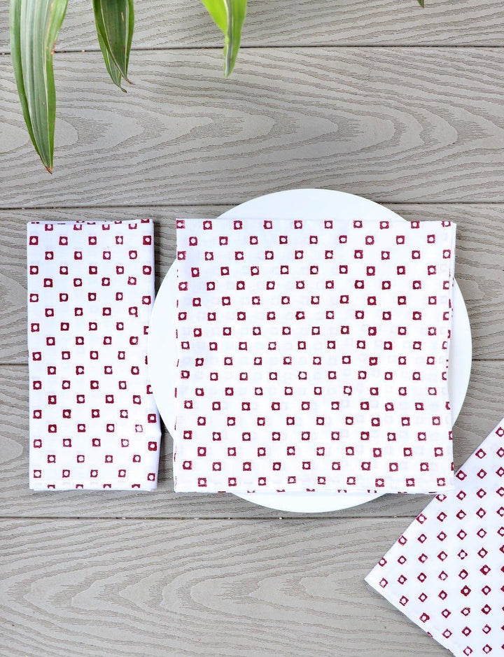 Set of four cotton napkins with a red square block print, folded.