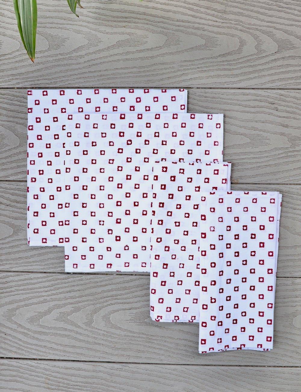 Set of four cotton napkins with a red square block print, folded.